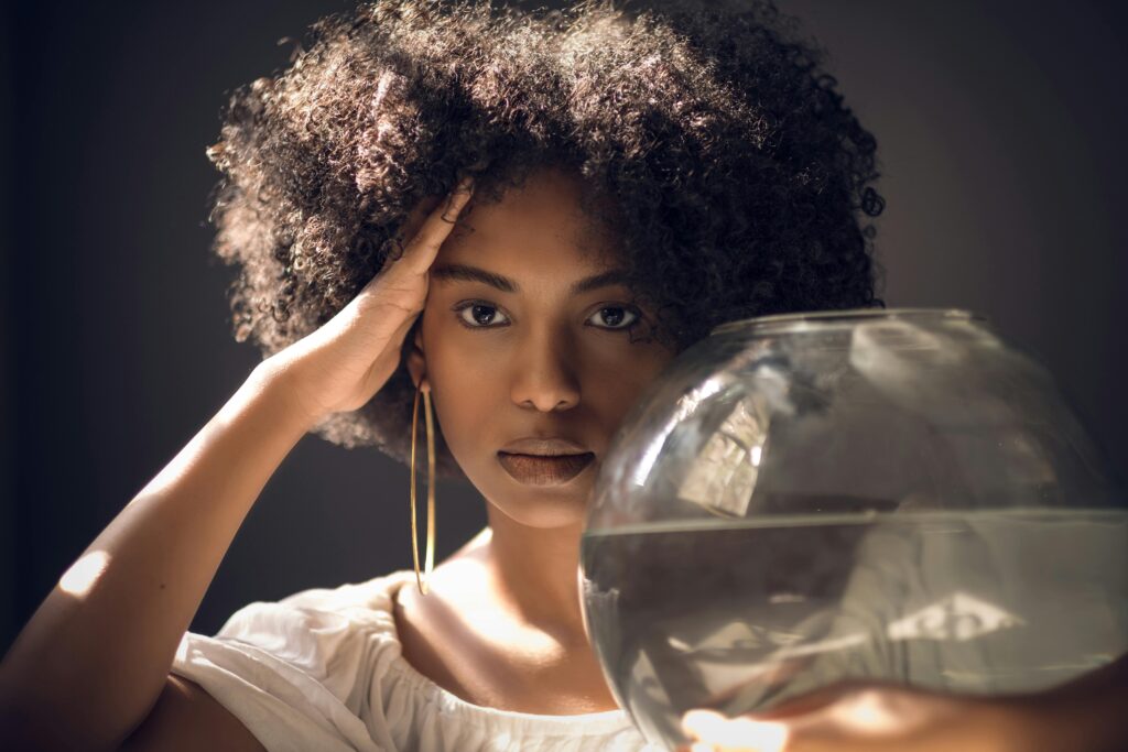 Elegant portrait of a woman with an afro holding a fishbowl indoors.