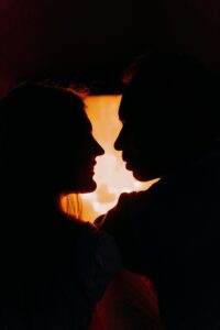 Silhouette of a couple sharing an intimate moment by a warm, glowing fireplace.